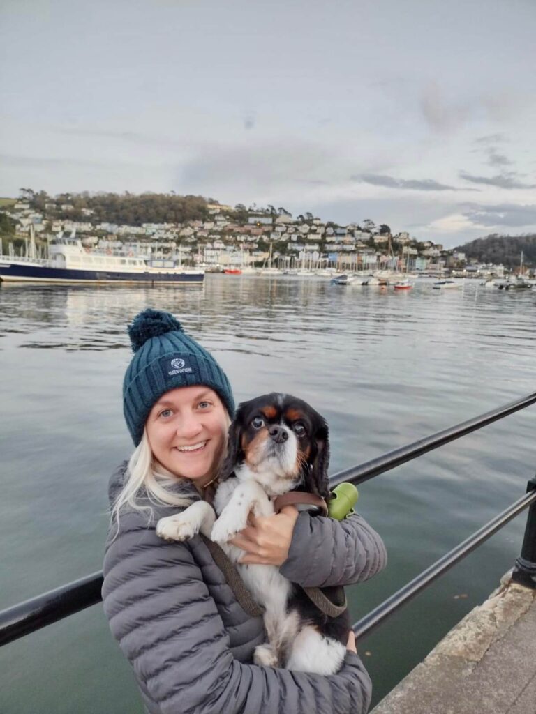 Woman holding dog standing in front of Dartmouth Harbour