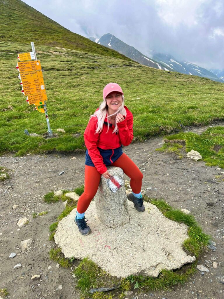 Woman wearing hiking clothes straddling the border between Switzerland and France