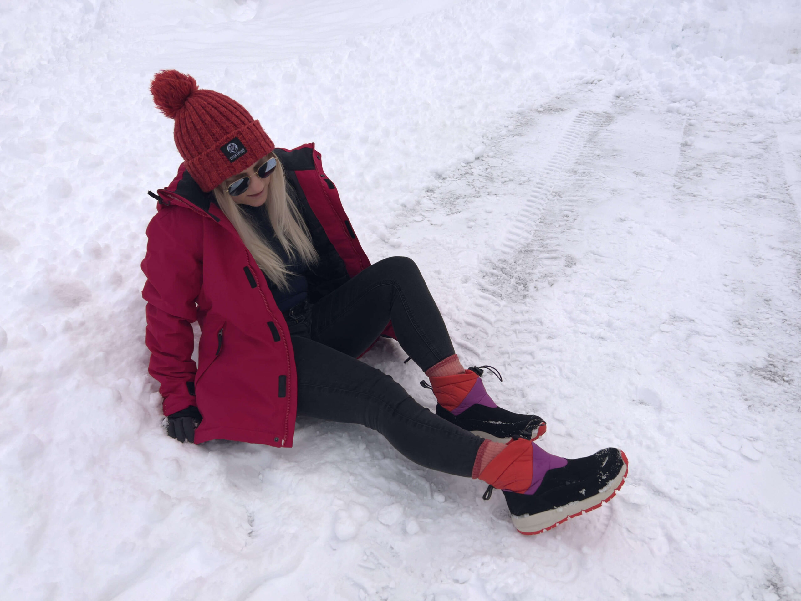 Sam sitting in the snow wearing snow boots and a ski jacket.