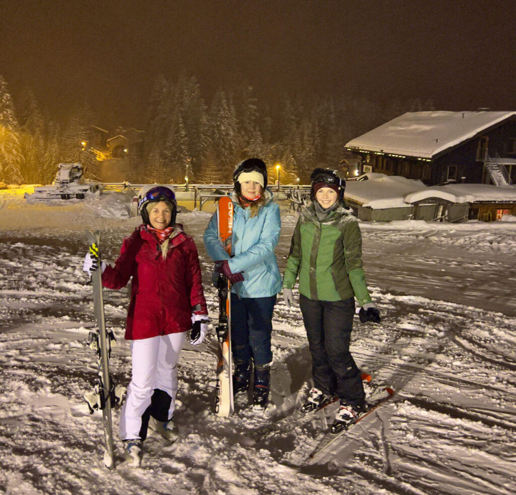 Three women pose with their skis during night skiing in Switzerland.