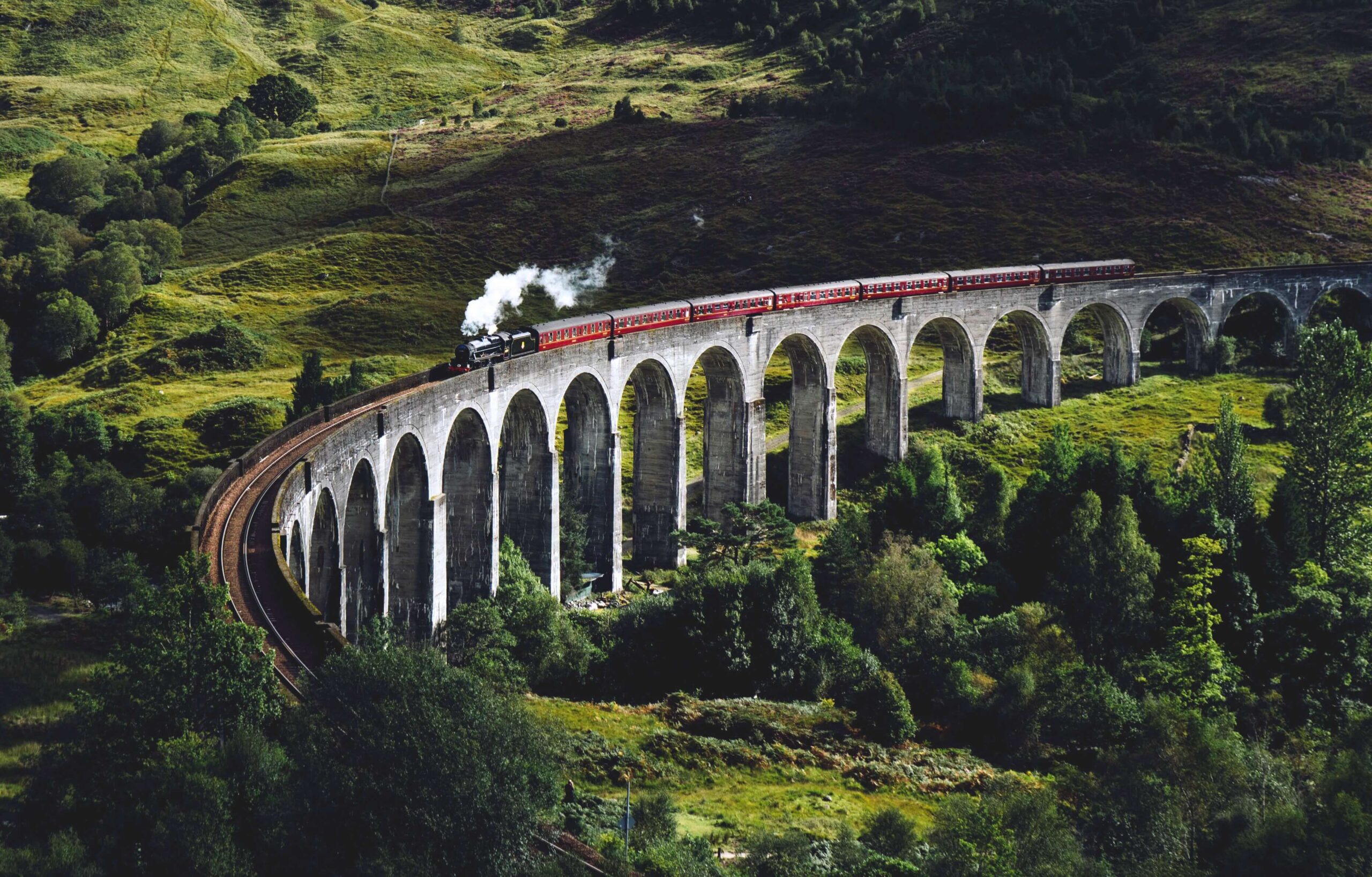 A steam train travels over Glen Finnan Viaduct in Scotland.