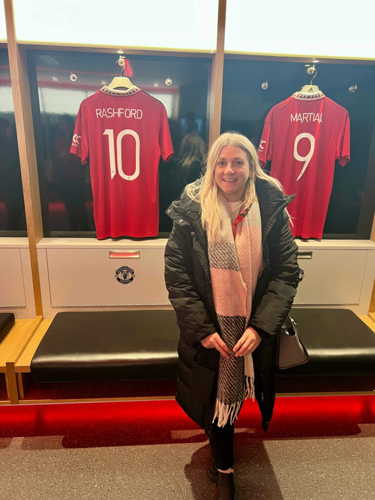 Sam standing in front of Rashford and Martial shirts in the Manchester United dressing room.