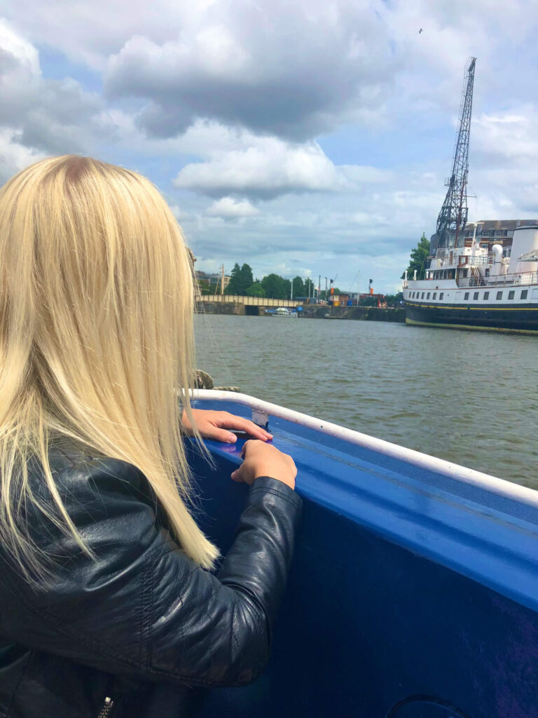 Sam looks out over the side of a boat on a boat trip in Bristol.