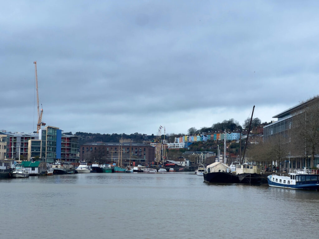 Boats in Bristol Harbour with a row of colourful houses behind them.