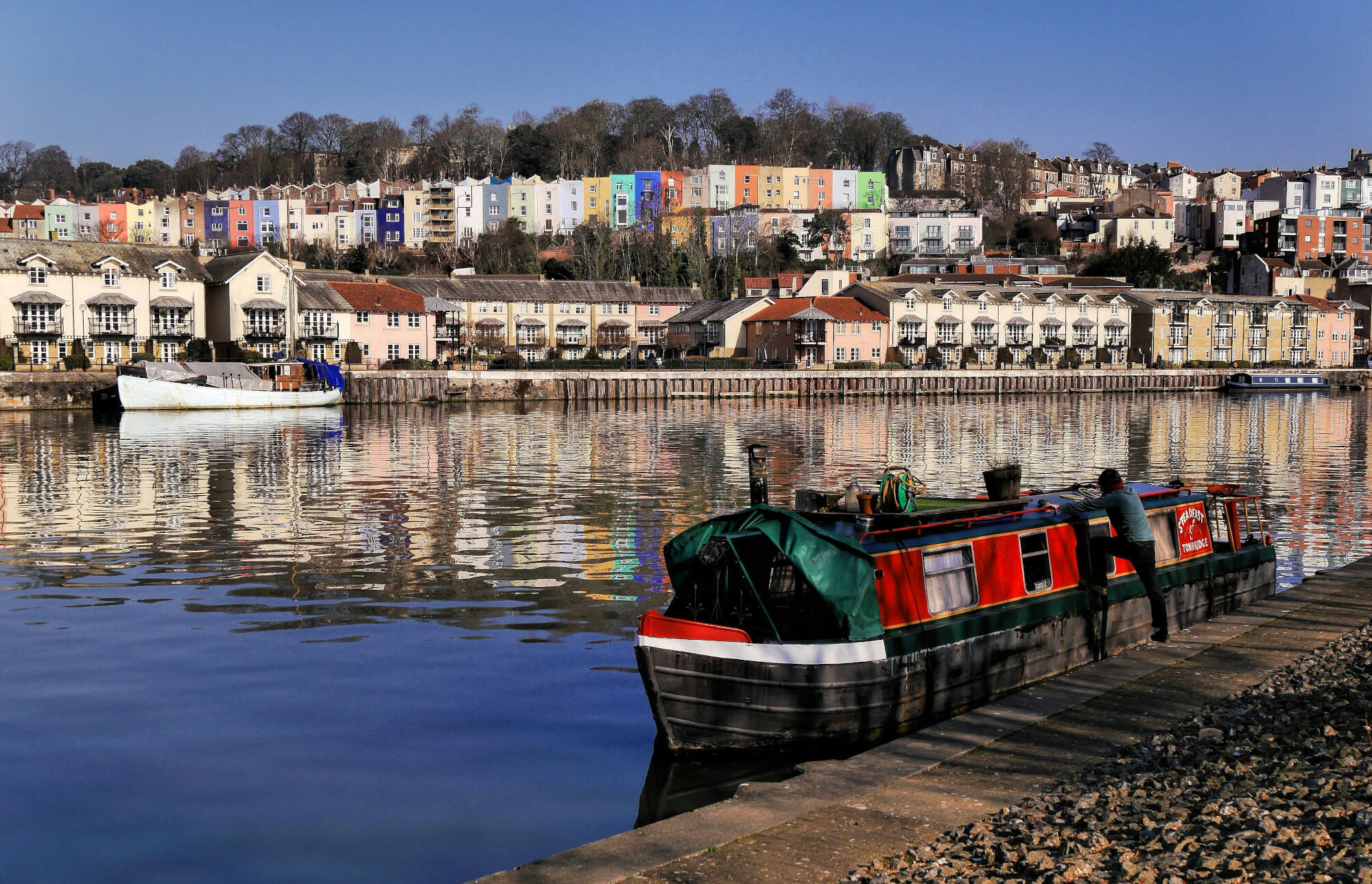 A large barge in Bristol Harbour, with colourful houses in the background.