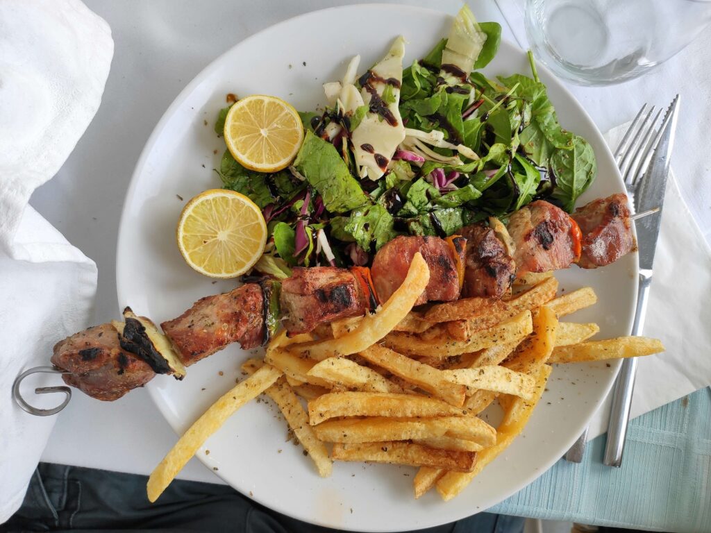 Greek kebab on a plate with salad and chips.