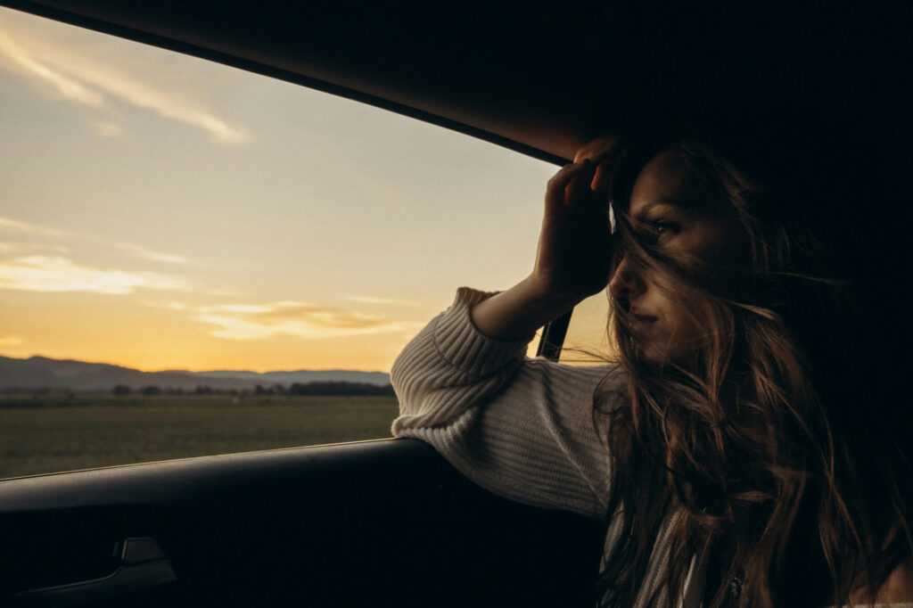 Woman looks out the window in the back of a car.