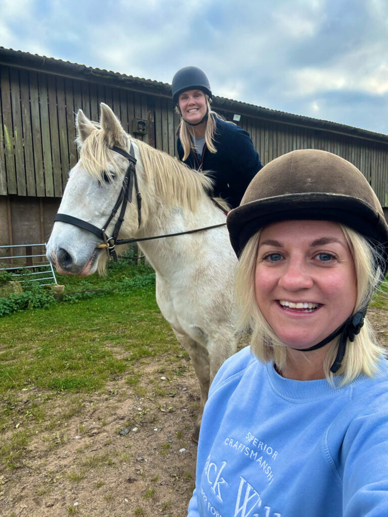 Sam and Fran take a selfie with their riding hats on. Fran is on a white horse.