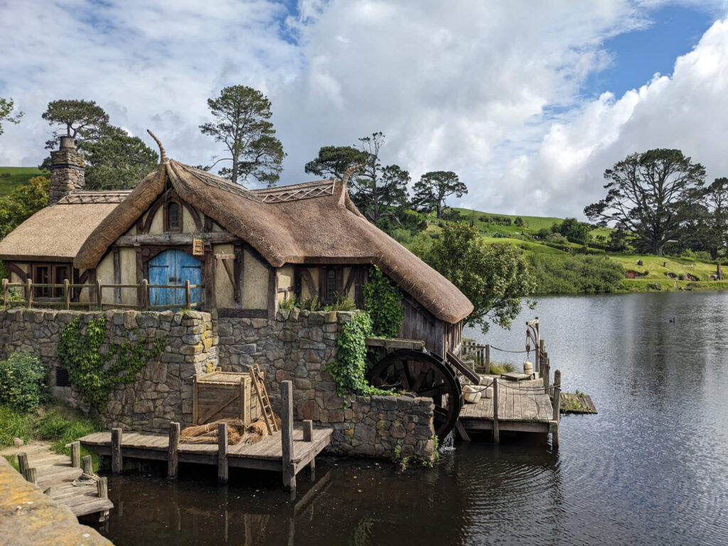 A house with a thatched roof on the river at Hobbiton in New Zealand.