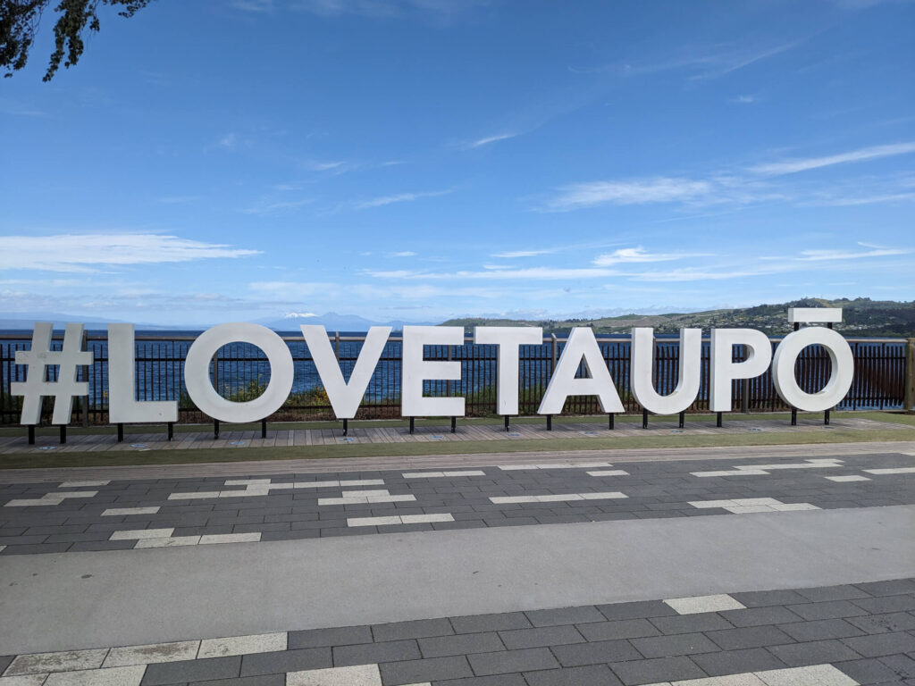 A sign reading "#LOVETAUPO" at Lake Taupo in New Zealand.