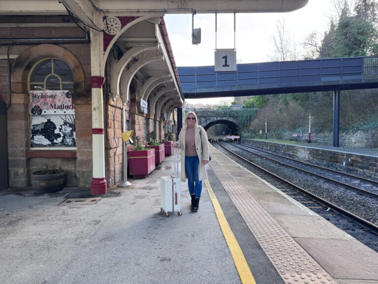 Sam standing with her cream Tavoxda carry on suitcase at the train station.