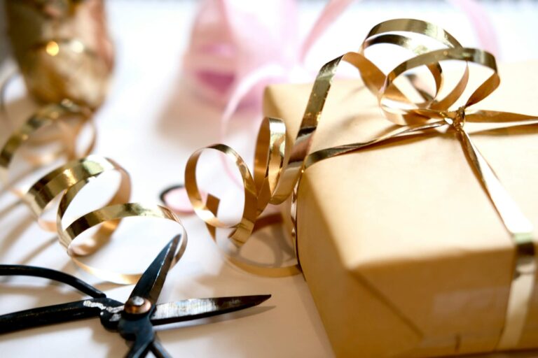 A box-shaped present wrapped in brown paper with a shiny gold bow around it. Scissors lie next to it.