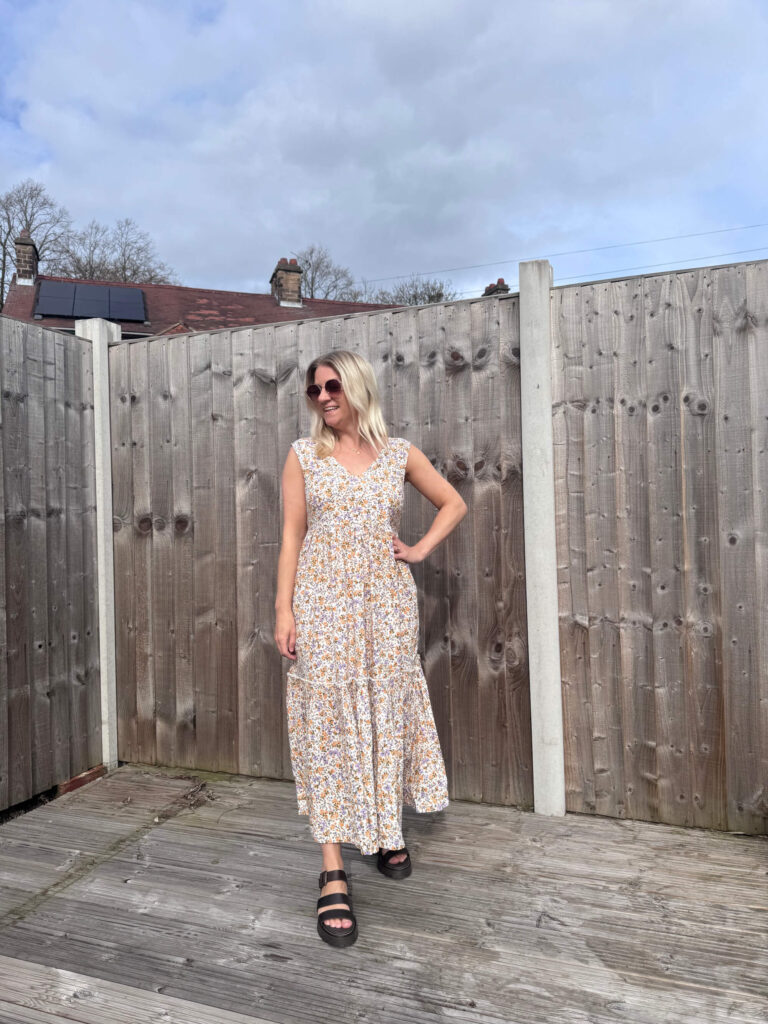 Sam wearing a floral midi dress with her hand on her hip.