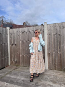 Sam wearing a floral midi dress with a faded denim jacket hanging off the shoulders.