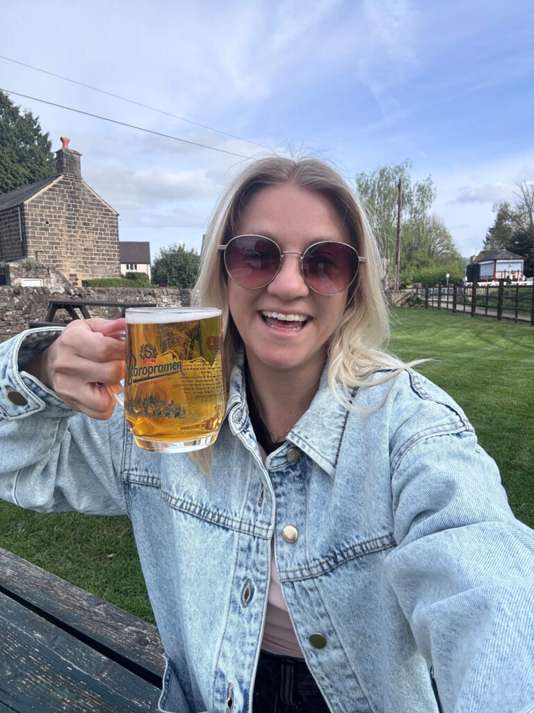 Sam wearing a faded denim jacket, holding a half pint of cider up to the camera.