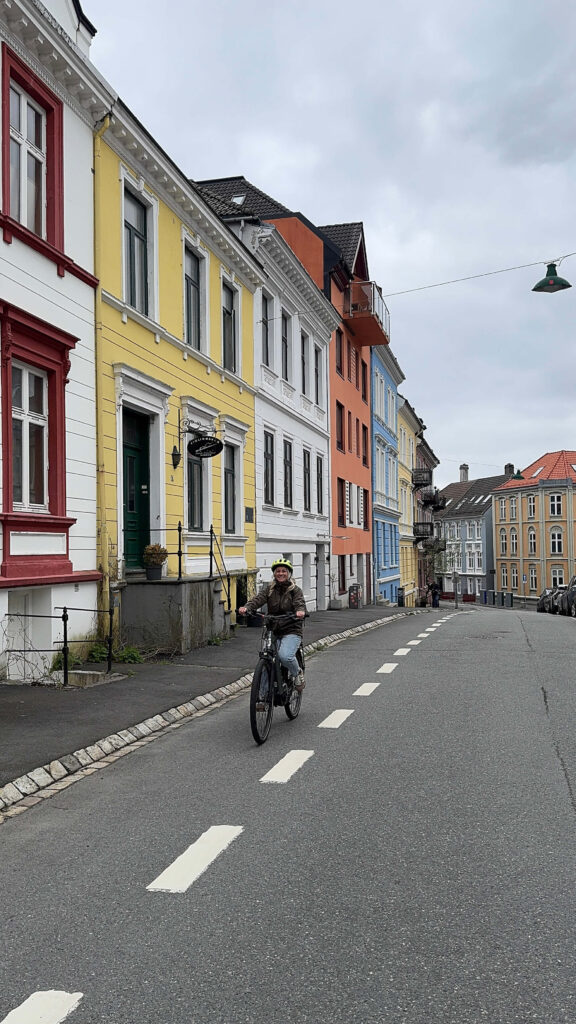 Sam riding an ebike through a street of pretty coloured houses in Bergen.