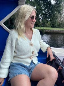 Sam sat on the back of a boat wearing a cream cardigan and shorts.