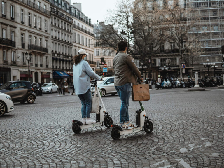Two people riding scooters through Paris.