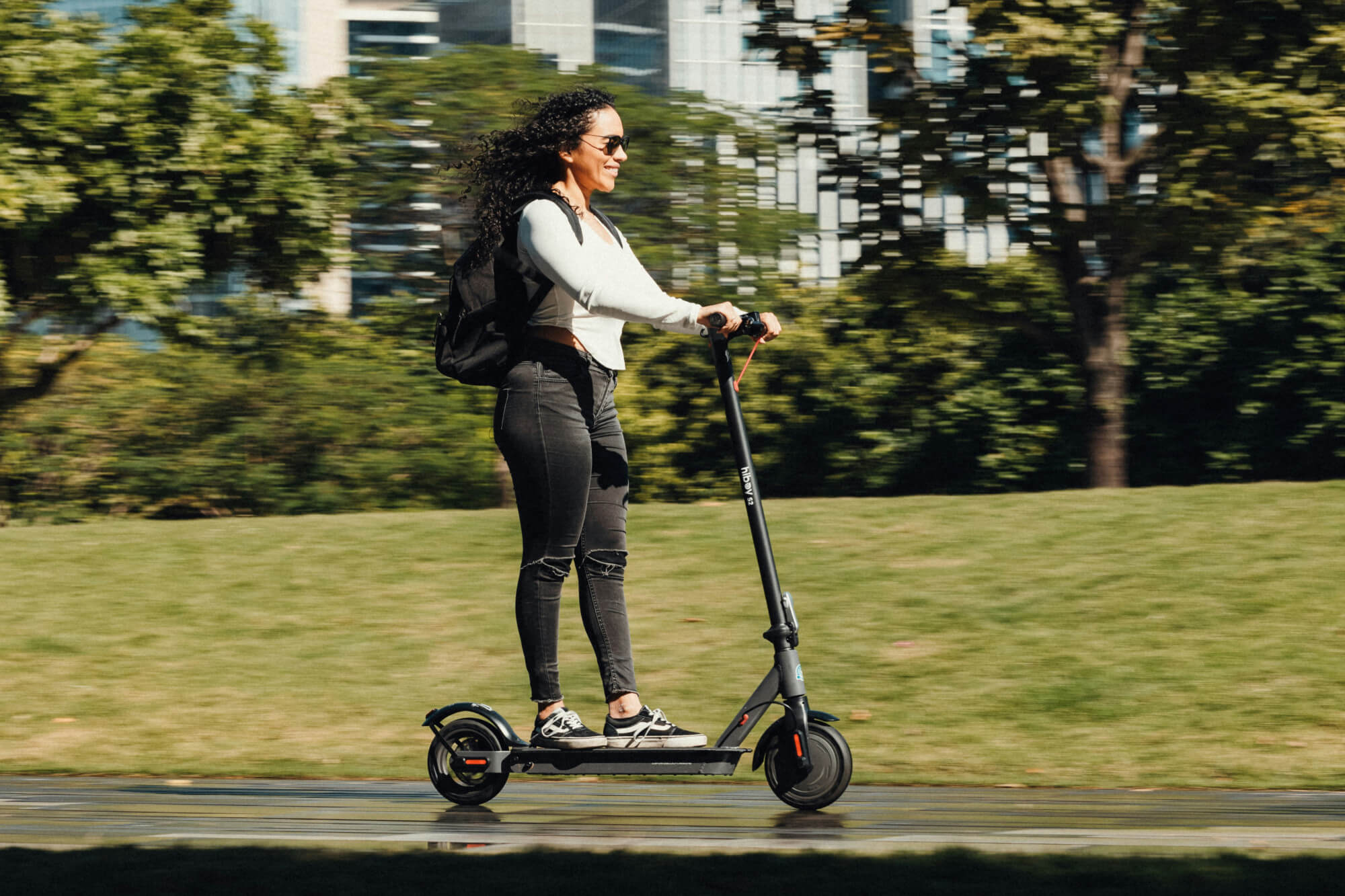 A woman riding an electric scooter on a path in a city park.
